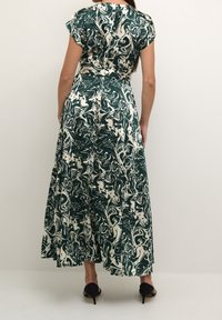 Grön och krämfärgad mönstrad maxiklänning med cinchad midja, korta ärmar och en flödande kjol. Bärs med svarta klacksandaler.