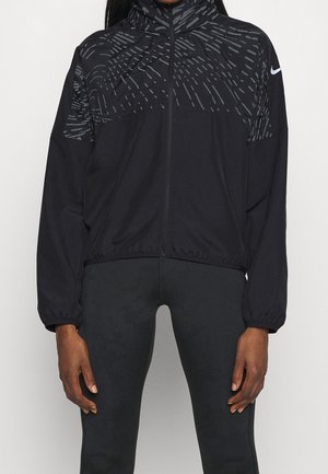 Black full-zip athletic jacket with subtle gray pattern on shoulders and sleeves, worn with black fitted pants, white Nike logo on left sleeve.