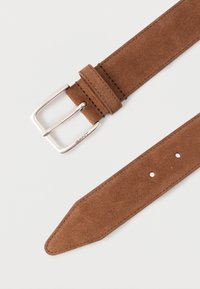 Καφέ σουέντ ζώνη με ασημένια μεταλλική αγκράφα, με ραφές και πολλαπλές τρύπες για ρύθμιση, με κωνικό σχέδιο στο άκρο.