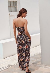 Kwiatowa, bezrękawnikowa sukienka maxi w ciemnym granacie, z dopasowanym gorsetem, lejącym się dołem i bocznymi kieszeniami. Noszona z czarnymi sandałami.