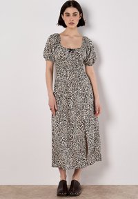 Maxikleid mit Leopardenmuster, Puffärmeln, quadratischem Ausschnitt und tailliertem Design; hat einen Schlitz vorne. Getragen mit dunklen, klobigen Clogs mit Absatz.