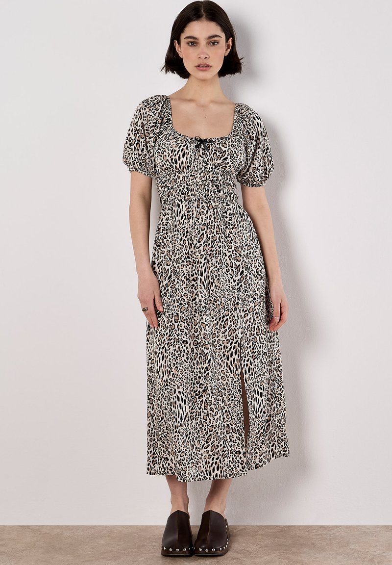Maxikleid mit Leopardenmuster, Puffärmeln, quadratischem Ausschnitt und tailliertem Design; hat einen Schlitz vorne. Getragen mit dunklen, klobigen Clogs mit Absatz.