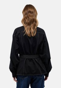 Vêtement d'extérieur noir avec une taille ceinturée, présentant des coutures contrastantes blanches, des manches amples et un design de dos structuré.