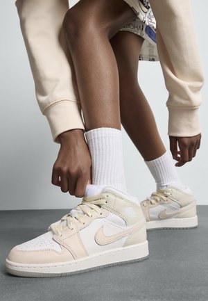 Baskets en cuir beige et crème avec une semelle en caoutchouc blanc et des accents beige clair. Des lacets blancs et des chaussettes complètent le look.