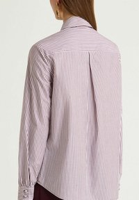 Camicia a maniche lunghe con righe verticali bordeaux e bianche, caratterizzata da una piega posteriore e polsini con bottoni, realizzata in tessuto leggero.