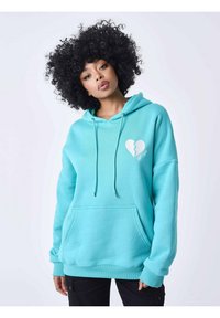 Sudadera turquesa con un bolsillo frontal, cordones y un gráfico de un corazón roto en el pecho. Fabricada con un tejido suave y texturizado.