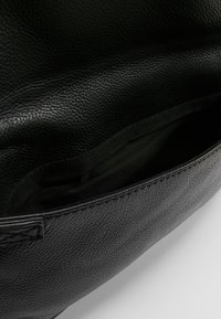 Interno di una borsa in pelle nera con una superficie texturizzata, caratterizzato da una fodera scura e una tasca laterale per l'organizzazione.