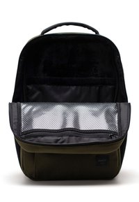 Sac à dos vert en tissu avec un intérieur noir, comprenant un compartiment rembourré et une poche en maille argentée avec une fermeture éclair. Poignées sur le dessus.