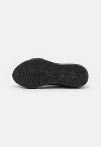 Semelle de chaussure noire en caoutchouc avec des motifs texturés, y compris des rainures et des crêtes pour la traction. Forme arrondie avec un talon légèrement surélevé.