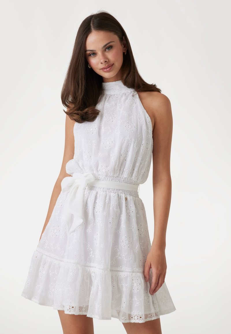 White dress with intricate embroidery, sleeveless design, high neckline, elastic waistband, and ruffled hem. Features a fabric belt.