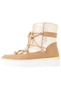 Stivaletto in suede beige con parte superiore in metallo dorato, caratterizzato da un layout con lacci e una suola piatta bianca con accenti dorati.
