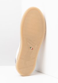 Tan Gummisohle mit strukturierter Griffmuster, versehen mit einem Etikett, auf dem "Made in Italy" und die Größe "42" steht. Glatte weiße obere Kante.