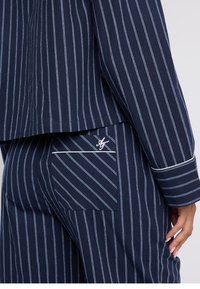 Navy striped loungewear set featuring vertical white lines, a pocket with an embroidered logo, and contrasting trim on the sleeves.
