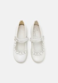 Witte leren Mary Jane-schoenen hebben een gestructureerde afwerking, een ronde neus en een bloemenapplicatie rond de band. Verstelbare band voor de juiste pasvorm.