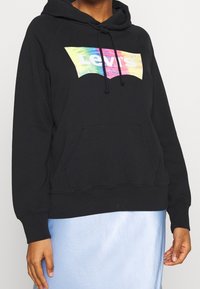 Hoodie nero con tasca a canguro e cappuccio con cordino. Presenta un logo Levi's colorato sul davanti, con una texture morbida simile al cotone.