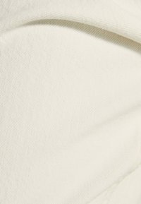 Látka krémové barvy s hladkou texturou, s mírným leskem a jemným diagonálním vzorem tkaní. Jsou viditelné pomačkané části.