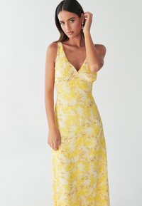 Yellow maxi dress featuring a floral pattern with light and dark yellow shades, V-neckline, and thin shoulder straps. Smooth fabric texture.