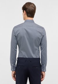 Maritiem patroon shirt met een geometrisch ontwerp, lange mouwen en knoopmanchetten, gecombineerd met donkere broeken. Glad stofoppervlak zichtbaar.