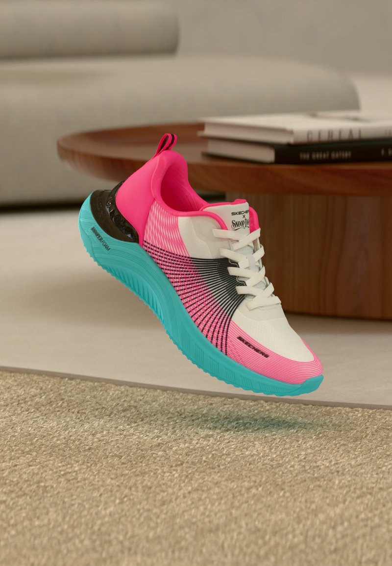 Ροζ, λευκό και μαύρο αθλητικό παπούτσι με φωτεινή μπλε σόλα, λευκά κορδόνια και λογότυπο «Skechers x Snoop Dogg», να αιωρείται πάνω από μπεζ χαλί σε εσωτερικό χώρο.