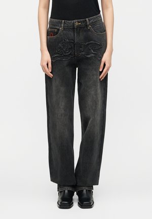 Osoba koja nosi široke tamnosive traperice s izvezenim obrubom zeca na prednjoj strani.