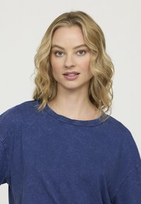 T-shirt à manches courtes bleu, avec une coupe ample et un col large, fabriqué à partir d'un tissu doux et texturé avec une finition délavée.