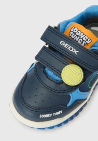 Barns marineblå joggesko med blått mesh, to borrelåsstropper merket GEOX, Looney Tunes-logo og en gul tennisball-detalj.