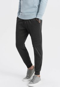 Donkergrijze joggingbroek met een tapered fit, elastische tailleband en zijzakken, gecombineerd met lichtgrijze sneakers. Zacht materiaal, casual ontwerp.