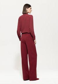 Maroon blouse with long sleeves and a collar, paired with wide-leg maroon trousers featuring back pockets and smooth texture.