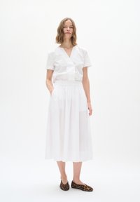 White short-sleeve blouse with a V-neck, paired with a white, flowy, ankle-length skirt featuring an elastic waistband. Brown leopard-print flats.
