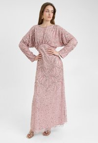 Roze lange jurk versierd met pailletten, met brede mouwen, een geraffineerde taille en ingewikkelde kraalpatronen. Heeft een vloeiende silhouet en een sheer overlay.