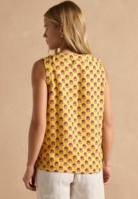 Varrukateta kollane bluus, millel on lillemuster roosade lilledega, valmistatud kergetest materjalidest. Lihtne, vabalt lasuuv disain.
