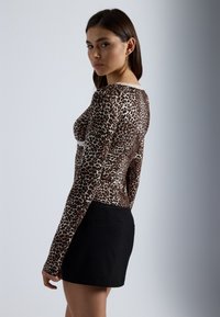 Μακρυμάνικη μπλούζα με σχέδιο λεοπάρ, με εφαρμοστό σχήμα και μαλακό ύφασμα. Συνδυάζεται με μαύρη κοντή φούστα.