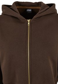 Brun zip-up hettegenser med gullglidelås, hette og myk, teksturert stoff. På innsiden er det foret med en kontrastfarge for ekstra detaljer.