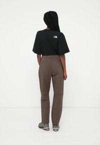 Czarny t-shirt z krótkim rękawem z małym białym logo z tyłu, połączony z brązowymi spodniami i szarymi butami trekkingowymi.