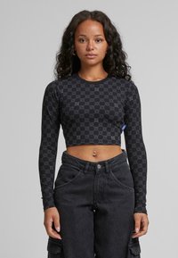 Fekete, hosszú ujjú crop top, geometrikus mintával, texturált anyagból és kerek nyakkivágással. Magas derekú fekete farmernadrággal párosítva.