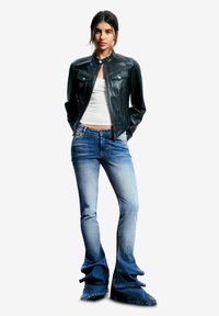 Chaqueta de cuero negra con cuello alto, dos bolsillos en el pecho, combinada con vaqueros acampanados azul claro con bajos deshilachados y diseño desgastado.