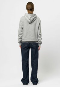 Grijze hoodie met een trekkoord capuchon, gecombineerd met loszittende donkerblauwe denim jeans. Opvallende details zijn de ribgebreide manchetten en het casual ontwerp.