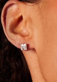 Boucles d'oreilles en cristal carré, montées sur un métal doré, vue en gros plan, mettant en valeur la clarté scintillante et les surfaces lisses.