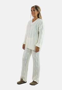 Completo da casa bianco lavorato a maglia con maglione oversize a scollo a V e pantaloni coordinati, caratterizzato da un design a trecce e polsini a coste.