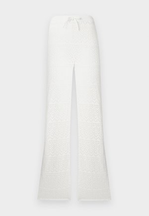 Pantalon en crochet blanc taille haute avec jambes évasées et ceinture à cordon sur un fond uni.