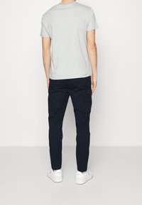 Man wearing light gray short-sleeve t-shirt, dark navy cargo pants, and white Polo sneakers, standing facing away on a plain white background.