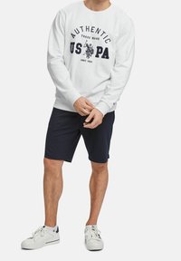 Bílá mikina s potiskem "AUTHENTIC US PA", spárovaná s námořnickými šortkami. Bílé tenisky s jemnými akcenty. Casual, sportovní design.