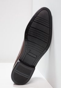 Semelle en cuir marron, semelle en caoutchouc avec texture striée, marquée de la taille 42. Présente des bords lisses et des éléments décoratifs minimaux.