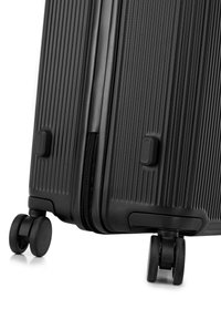 Black hard-shell suitcase with a textured surface, zipper closure, and two double wheels for mobility. Features horizontal lines and sturdy handles.