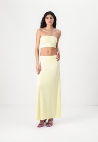 Yellow strapless top and matching long skirt, made of smooth fabric. Model wearing purple high-heeled sandals. Simple, fitted design.