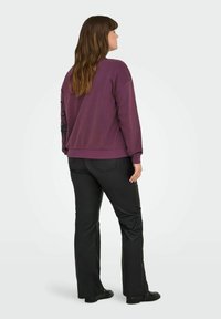 Sudadera morada con un corte relajado y puños de canalé, combinada con pantalones negros. La sudadera presenta un diseño floral en el brazo izquierdo.