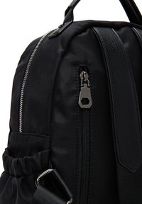 Zaino nero realizzato con una combinazione di nylon liscio e pelle testurizzata. Elementi notevoli includono una cerniera argentata e dettagli della tasca con cordoncino.