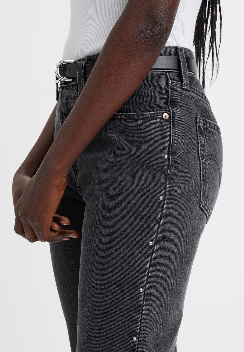 Jeans en denim noir avec une coupe droite, une texture subtile et des clous en argent décoratifs le long de la couture latérale. Ceinture à boucle en argent incluse.