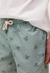 Shorts azzurri con un motivo di teschi e ossa incrociate, realizzati in tessuto morbido, con una vita elastica e un cordoncino.