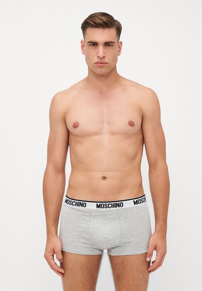 Sive bokserice z črno-belo Moschino elastiko. Tkanina se zdi mehka z gladko teksturo, prilega se telesu in nima vidnih vzorcev.